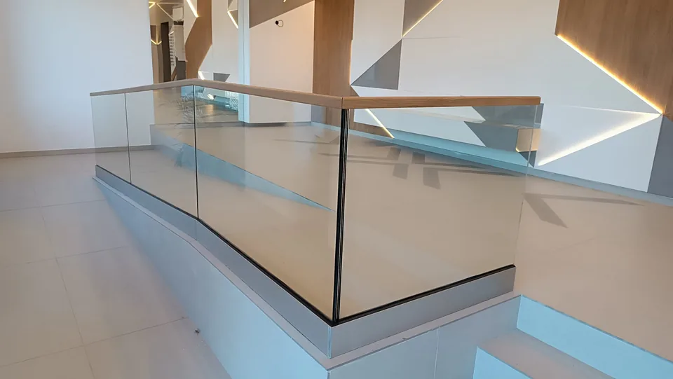 Parapet de sticlă cu mână curentă din lemn pe un palier interior.
