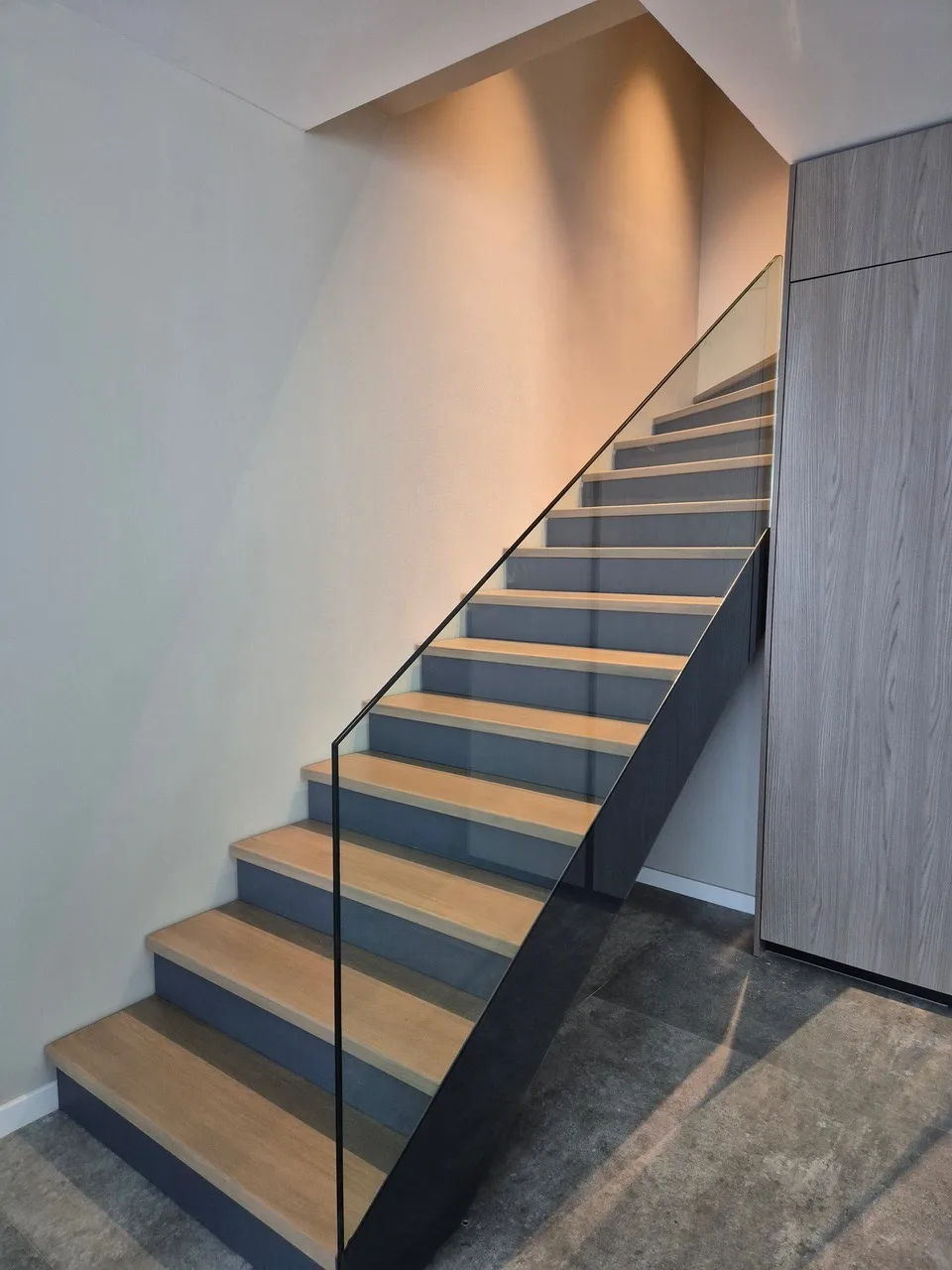 Balustradă transparentă pe o scară cu trepte din lemn și beton.