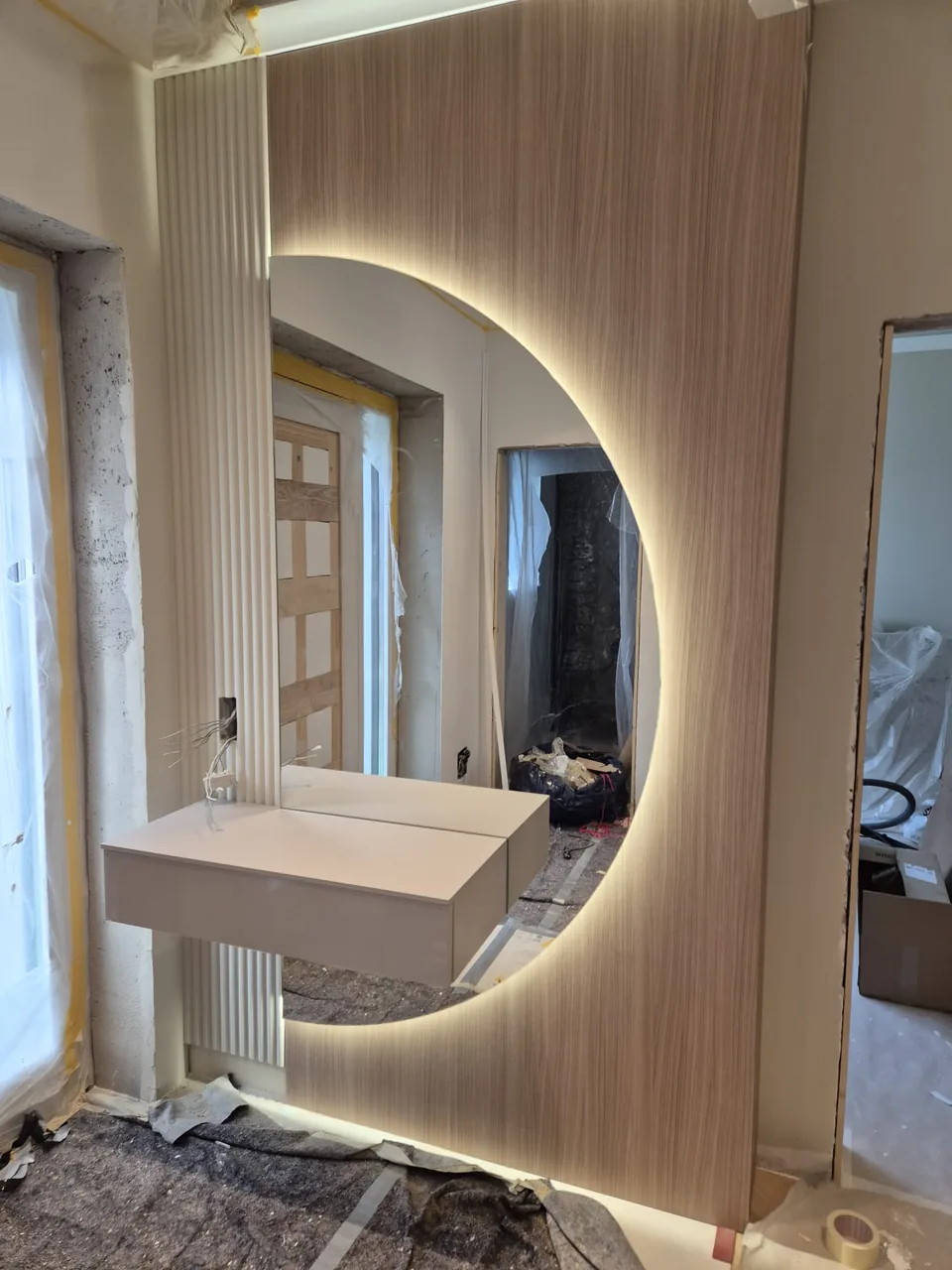 Oglindă rotundă cu iluminare perimetrală montată pe panou decorativ.
